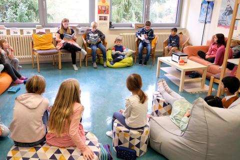 Am bundesweiten Vorlesetag sitzen in der Geschwister-Grimm-Schule drei Vorlesende in Korbstühlen, während die anderen es sich auf einer Couch oder Sitzkissen bequem machen. © Martin Fromme