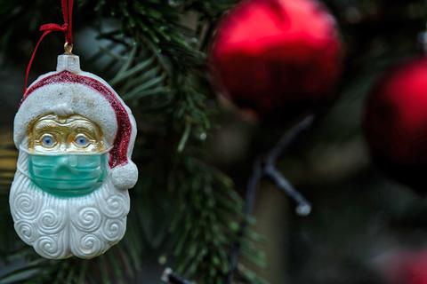Ein Weihnachtsmann mit Mund-Nasen-Schutz hängt als Baumschmuck an einem Weihnachtsbaum. Foto: Federico Gambarini/dpa