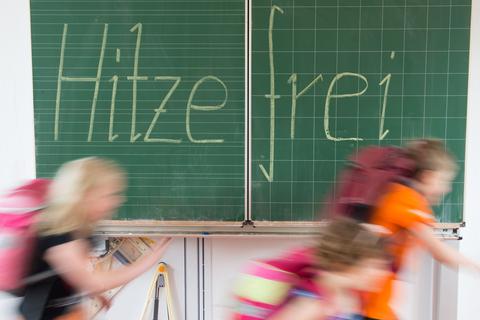 Schüler einer 2. Klasse laufen in einer Grundschule an einer Tafel mit der Aufschrift "Hitzefrei" vorbei. 