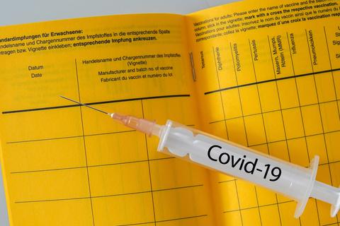 Eine Spritze mit der Aufschrift "Covid-19" liegt auf einem aufgeschlagenen Impfausweis.  Symbolfoto: Milton Oswald - stock.adobe